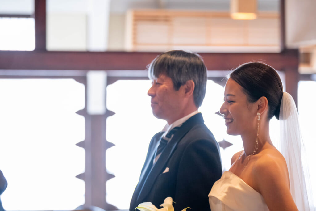 挙式直前、新婦と父親。新婦は父の横で幸せそうな表情を浮かべています。