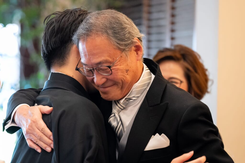 新郎と、そのお父様が固くハグを交わしている写真。お父様の表情から深い愛情と喜びが伝わる、感動的な瞬間。